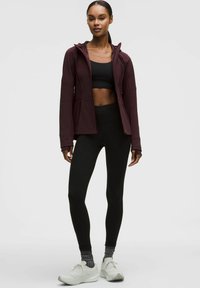 Idrottskläder som består av en vinröd zip-up jacka, en svart crop-top, svarta leggings och vita sneakers med grå accenter. Texturerad tyg synlig.