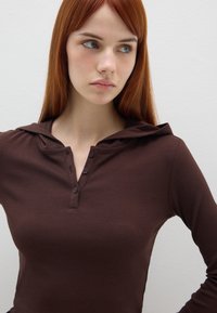 Top a maniche lunghe rigato marrone con colletto henley con bottoni e cappuccio incorporato. La texture liscia e il design aderente mettono in risalto la silhouette.