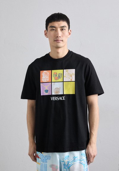 T-shirt in cotone nero con stampa grafica quadrata che presenta illustrazioni colorate e il logo "VERSACE" in basso. Vestibilità casual, maniche corte.