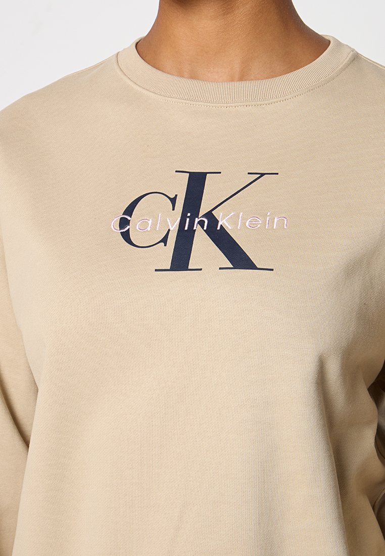 Beżowa bawełniana bluza z dużym granatowym logo "CK" oraz napisem "calvinKlein" w jasnoróżowym kolorze, z okrągłym dekoltem i ściągaczami.