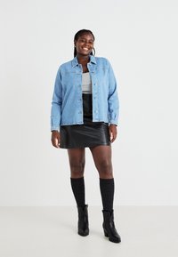 Gaišzila džinsa jaka ar pogu aizdari un krūšu kabatām, kombinēta ar pelēku topu, melnu ādas svārku un ceļgala auguma zeķēm.