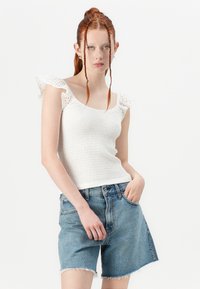 Witte smocktop met kant afgewerkte ruches aan de mouwen, gecombineerd met hoog getailleerde lichtblauwe denim shorts met een rafelige zoom.