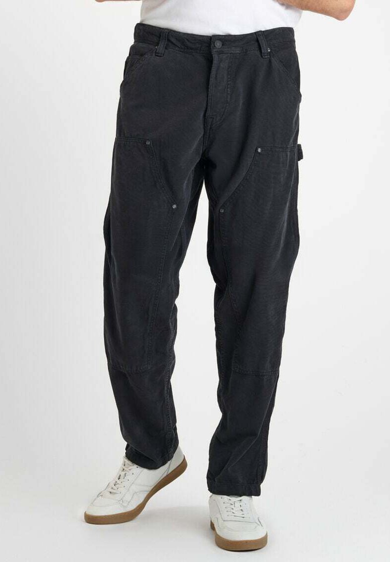Pantalons cargo noirs avec plusieurs poches, coupe décontractée, tissu texturé et fermeture à bouton sur le devant, associés à des baskets blanches.