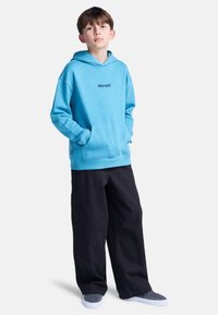 Felpa con cappuccio azzurro chiaro con tasca frontale e logo "element" nero, abbinata a pantaloni neri larghi e scarpe slip-on grigie. Tessuto morbido, vestibilità casual.