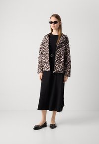 Jachetă cu fermoar, cu imprimeu leopard și glugă, purtată peste o rochie neagră. Pantofi negri cu talpă joasă și accente decorative completează ținuta. Ochelari de soare adăugați.