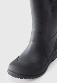 Botte en caoutchouc noir avec surface texturée, orteil renforcé et semelle crantée pour une meilleure traction. Présente une finition lisse et une construction robuste.