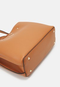 Sac à main en cuir tan avec une finition texturée, des accents en métal doré et quatre pieds en métal. Il présente une forme structurée avec un haut lisse et courbé.