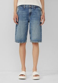 Shorts en denim bleu clair avec une finition délavée, présentant un design classique à cinq poches et un ourlet retroussé. Portés avec des sandales à plateforme de couleur claire.