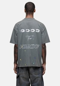 Szary, oversize t-shirt z napisem "GOOD FOR NOTHING" na plecach, z plamkami koloru i casualową, miękką fakturą.
