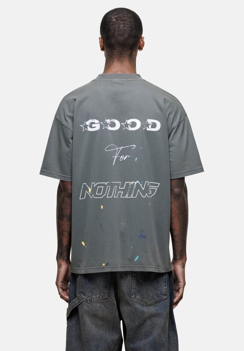 Szary, oversize t-shirt z napisem "GOOD FOR NOTHING" na plecach, z plamkami koloru i casualową, miękką fakturą.