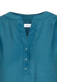 Blusa blu acqua con colletto rotondo con spacco, apertura a V e tre bottoni lungo la pattina frontale.