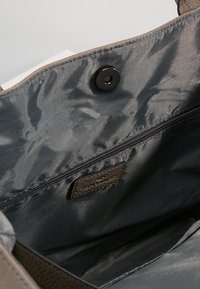 Interiér hnědé tašky s hladkou texturou, vybavený tmavě šedou podšívkou, kapsou na zip a detailem s patentním uzávěrem.