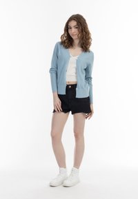 Cardigan din tricot de culoare albastru deschis, cu un model texturat, purtat peste un top alb scurt, asortat cu șorturi din denim negre și adidași albi cu glezna înaltă.