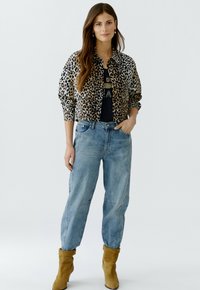 Leopardenmuster gefütterte Jacke, schwarzes Oberteil, hellblaue weite Jeans und braune Stiefeletten. Die Jacke hat ein Knopfdesign mit elastischen Bündchen.