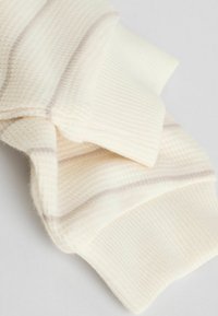 Primer plano de una tela de punto color crema con puños acanalados y sutiles rayas horizontales en tonos beige claros.