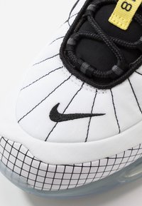 Nike-sneaker med en vit ovandel med svart sömnad och rutmönster, svarta accenter och en synlig luftenhet i sulan.