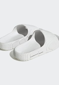 Vita slip-on sandaler med ribbat mönster och öppen design. Har ett subtilt präglat mönster och varumärke längs sidan.