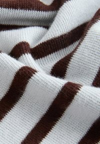 Tissu tricoté doux avec des rayures horizontales épaisses alternantes marron et blanches, présenté en gros plan avec une texture et des plis visibles.