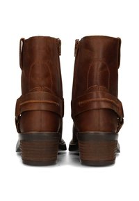 Stivali ankle in pelle marrone con una texture liscia, zip sul retro e una sottile tracolla sulla parte superiore. Design con tacco spesso e impilato.