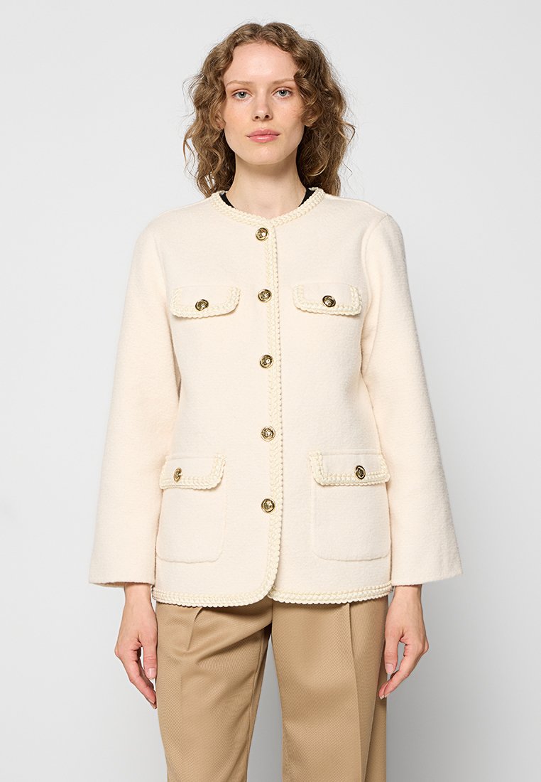 Cremfarbener Wolljacke mit rundem Ausschnitt, drei goldenen Knöpfen, zwei vorderen Taschen mit geflochtenen Akzenten und einer glatten Textur.
