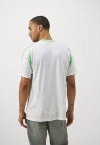 Maglietta sportiva bianca con dettagli verdi, maniche corte e una texture a rete nella parte inferiore. Presenta un design a colletto rotondo.