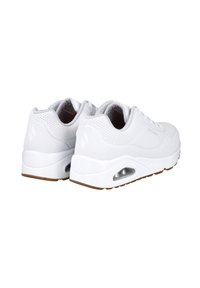 Zapatillas deportivas blancas con una parte superior perforada, suela acolchada y ventana de aire transparente en el talón; suela de goma con un patrón texturizado.