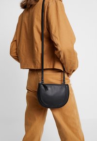 Borsa a tracolla nera in pelle, a forma di mezzaluna, con texture liscia e chiusura zippata. Presenta una tracolla sottile e regolabile.