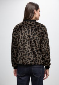 Leopard print fleece jacket with a soft texture, black ribbed cuffs and hem, and a relaxed fit. Visible stitching on dark denim jeans.