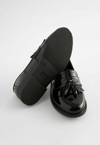 Loafers din piele lăcuită neagră cu detaliu de ciucure, talpă plată din cauciuc și un finisaj neted și lucios. Marcajele de mărime și brand sunt vizibile pe talpă.