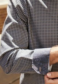 Homme ajustant le poignet d'une chemise à manches longues à motifs avec un design floral contrastant sur le poignet.