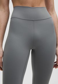 Korkeavyötäröiset harmaat legginsit, jotka on valmistettu joustavasta materiaalista, ja niissä on litteät saumat ja sileä pinta. Suunniteltu mukavuutta ja liikkuvuutta varten.