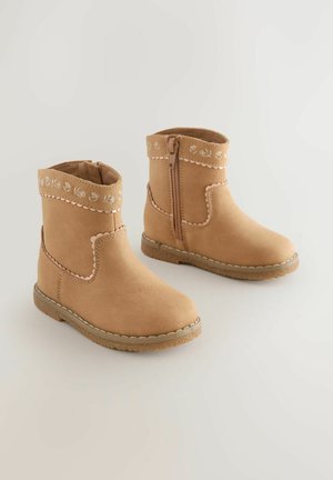 Krémové semišové členkové topánky s vyšívaným kvetinovým vzorom na vrchu, bočným zipsom a textúrovanou gumovou podrážkou, s jemne prešitým dizajnom.