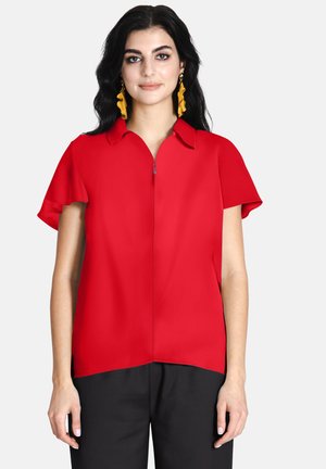 Blusa rossa a maniche corte con colletto a punta e zip parziale sul davanti, caratterizzata da una texture liscia e una vestibilità rilassata.