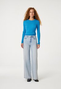 Blauw ribbed langemouwen top gecombineerd met lichtblauwe wijdvallende jeans. De outfit heeft een getailleerde taille en een relaxed fit van de heupen naar beneden.