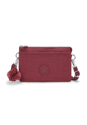 Sac en bandoulière en tissu rouge avec fermeture éclair, featuring un patch en relief avec logo et un porte-clés en fourrure de singe détachable.