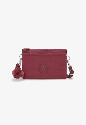 Červená crossbody taška se zipovým uzávěrem, která má texturovanou nášivku s logem a odnímatelný klíčenkový doplněk ve tvaru chlupatého opičáka.