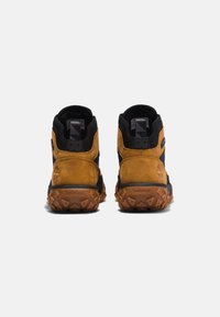 Par de botas Timberland en negro y marrón vistas desde atrás, con suelas resistentes y lengüetas de agarre, sobre un fondo blanco liso.