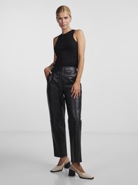Top preto sem mangas combinado com calças de pele de cintura alta e ajustadas. O conjunto inclui sapatos de salto slingback bege com um salto grosso.
