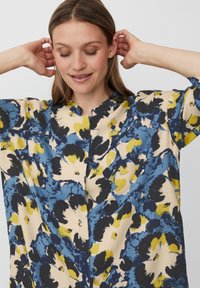 Bloemendesshirt met blauwe, gele en zwarte tinten. Gemaakt van lichtgewicht stof, heeft het een relaxte pasvorm en een staande kraag.