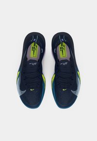Para granatowo-niebieskich butów do biegania Nike z akcentami w kolorze limonki i zieleni, widziane z góry na białym tle.