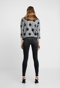 Suéter gris con grandes lunares negros, mangas tres cuartos, combinado con jeans ajustados oscuros y tacones altos negros.