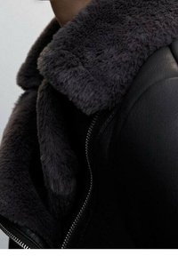 Czarna skórzana kurtka z grubym, puszystym szarym kołnierzem i gładką fakturą. Widoczny zamek błyskawiczny z przodu.