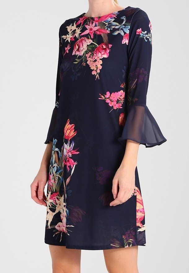 Robe bleu marine avec imprimé floral rose et orange, manches évasées transparentes et coupe droite longueur genou portée par une personne debout.
