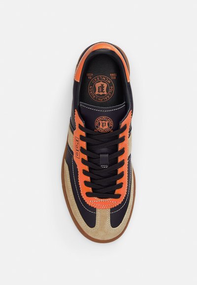 Sportbačiai su tamsiai mėlynos odos, oranžiniais akcentais ir smėlio spalvos zomšu. Juodos raištelės, guminis padas ir logotipo lopas ant liežuvio.