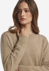 Beżowy sweter z dzianiny z okrągłym dekoltem, ściągaczami przy rękawach i miękką fakturą, charakteryzujący się luźnym krojem i subtelnymi detalami w szwie.