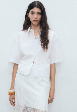 Witte korte mouwen blouse met een relaxed fit, gecombineerd met een witte kanten rok. De outfit heeft een soepele textuur en lichte stof.