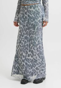 Gonna maxi in un tessuto leggero e trasparente con stampa leopardata grigia. L'orlo è ondulato, abbinata a stivali neri alla caviglia.