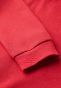 Gros plan sur la manche d'un sweat-shirt rouge montrant le poignet côtelé et la texture lisse du tissu.