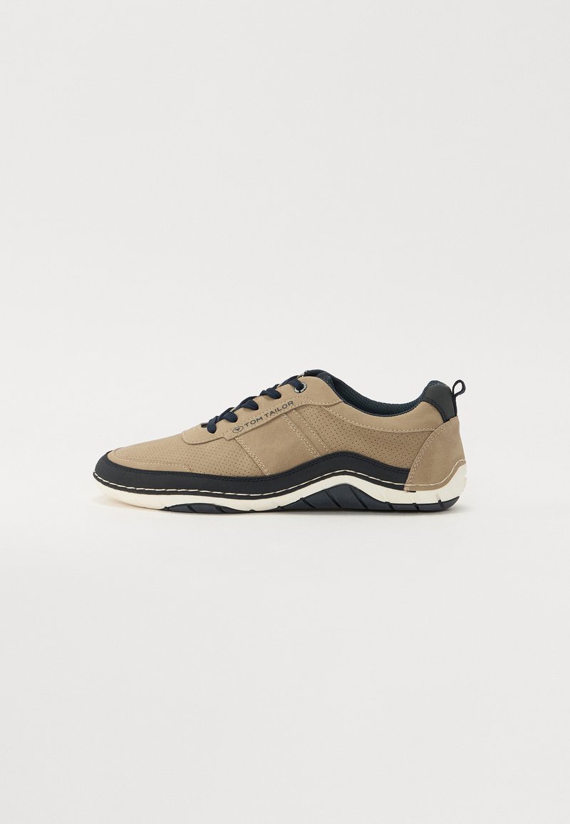 Beige Sport-Schuh aus strukturiertem Stoff mit marineblauen Akzenten und weißer Sohle. Verfügt über Schnürsenkel, Nähdetails und ein konturiertes Design.
