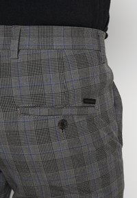Pantalon à carreaux noir et gris avec des accents bleus. Comprend un bouton noir et une poche arrière. Texture lisse. Design sur mesure.